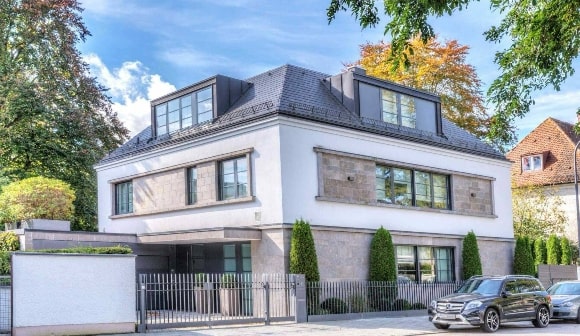 Moderne weiße Stadtvilla mit Natursteinelementen, Toreinfahrt und geparkten Autos in München