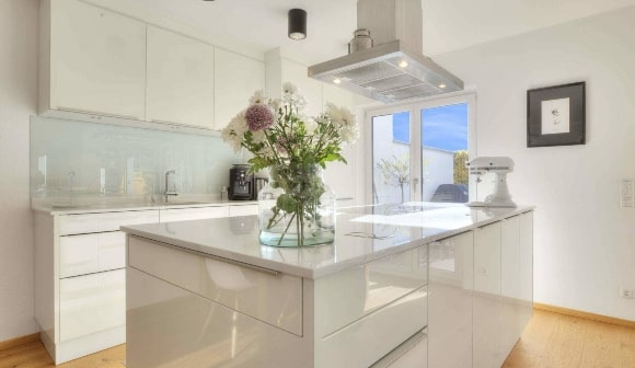 Moderne weiße Hochglanzküche mit großer Kücheninsel und Blumenstrauß in einer Münchner Immobilie