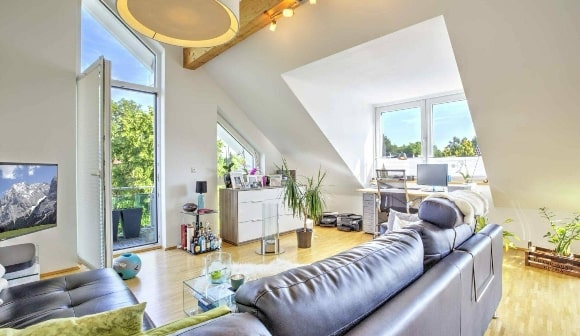Helles Dachgeschosswohnzimmer mit dunklem Ledersofa, Schrägen und Zugang zum Balkon in München