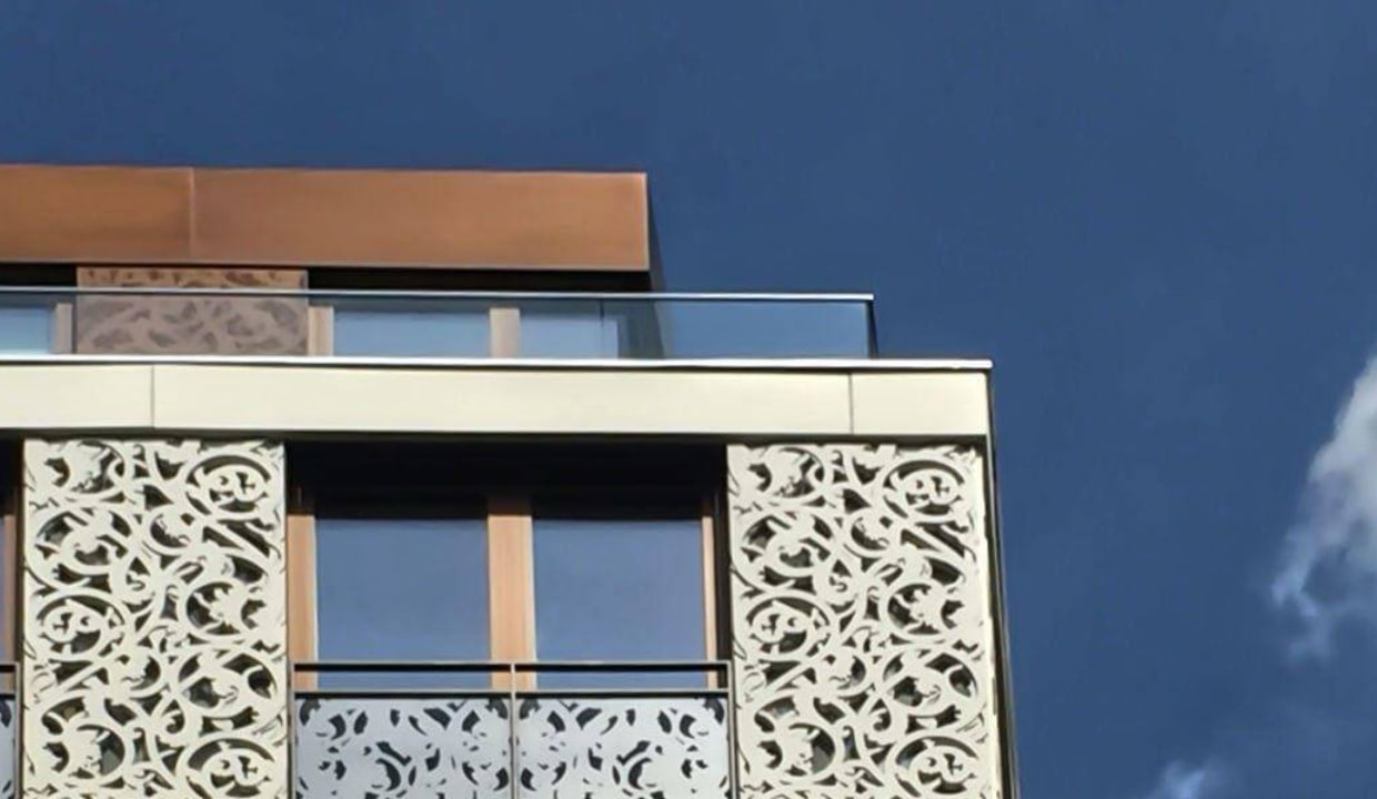 Detailaufnahme einer modernen Fassade mit ornamentalen Balkongittern vor blauem Himmel in München