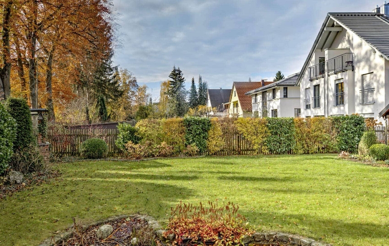 Weitläufiger gepflegter Rasengarten mit herbstlich gefärbten Bäumen vor einer weißen Villa mit Erker.
