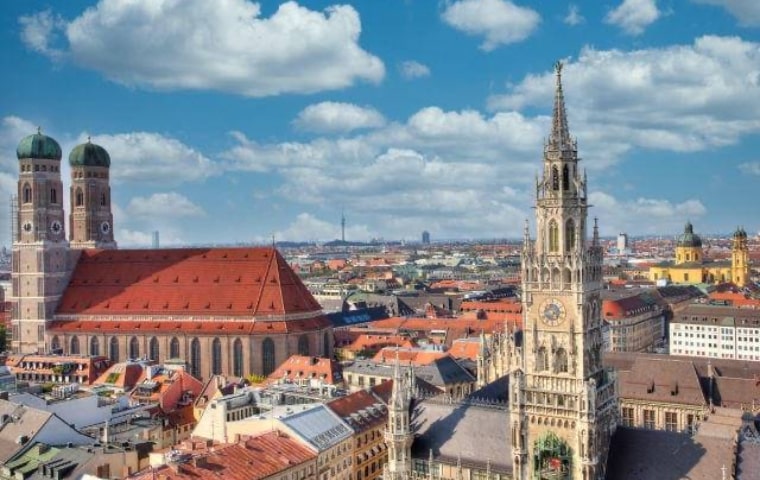 Panoramablick über München mit den Türmen der Frauenkirche und dem Turm des Neuen Rathauses vor Wolkenhimmel
