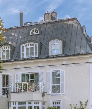 Historisches Altbaudach mit Gaube, Schieferdeckung und weißem Balkon-Erker unter blauem Himmel.