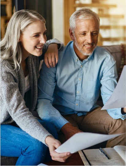 Lächelndes älteres Paar betrachtet gemeinsam Unterlagen, Symbolbild für Finanzierungsberatung bei Immobilien