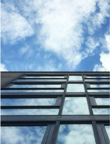Perspektivischer Blick nach oben an einer modernen Glasfassade vor bewölktem Himmel in München