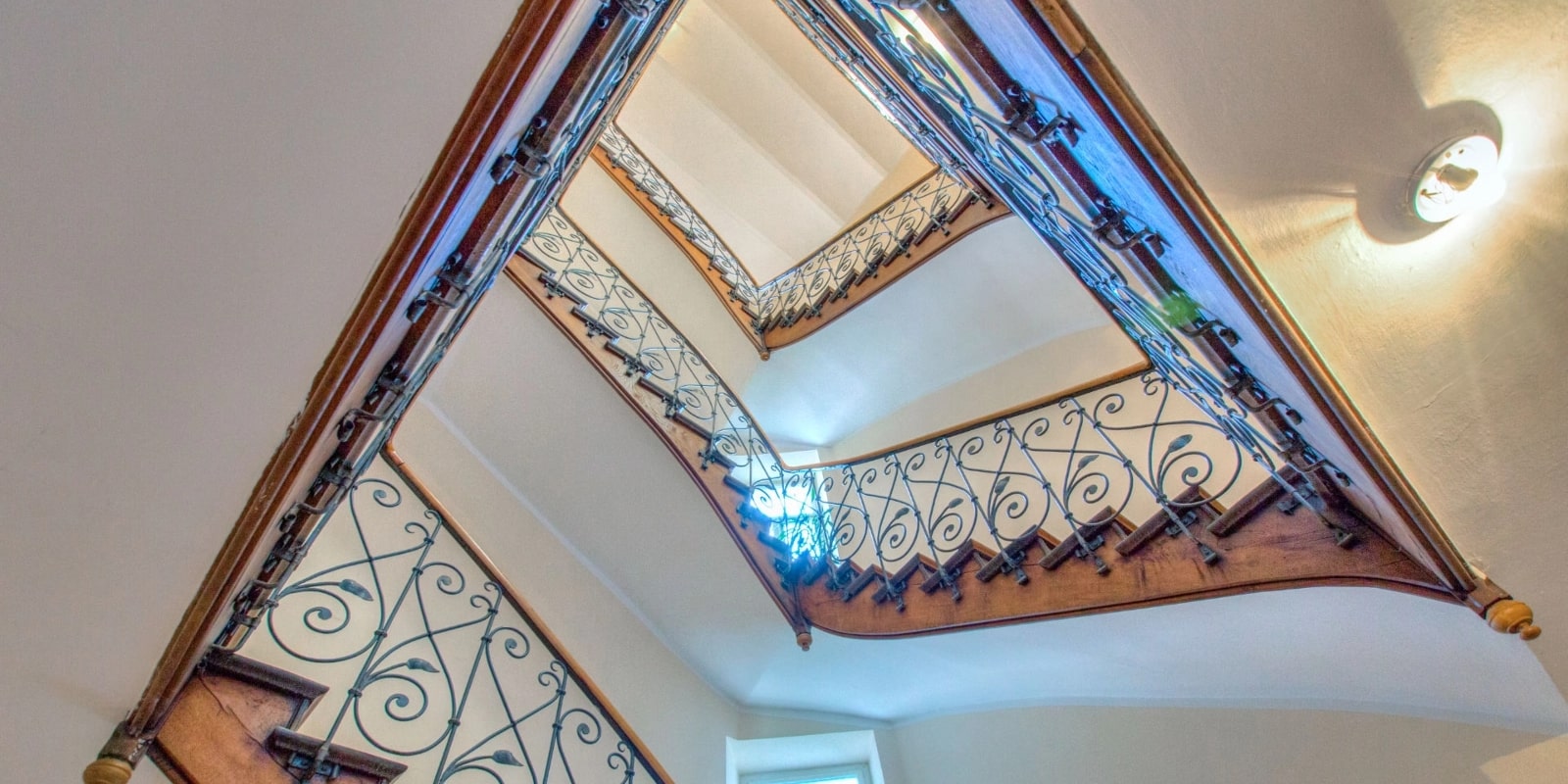 Blick von oben auf ein historisches Treppenhaus mit schmiedeeisernem Geländer
