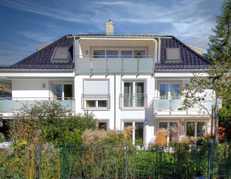 Weißes Mehrfamilienhaus mit dunklem Walmdach und Balkonen in Germering