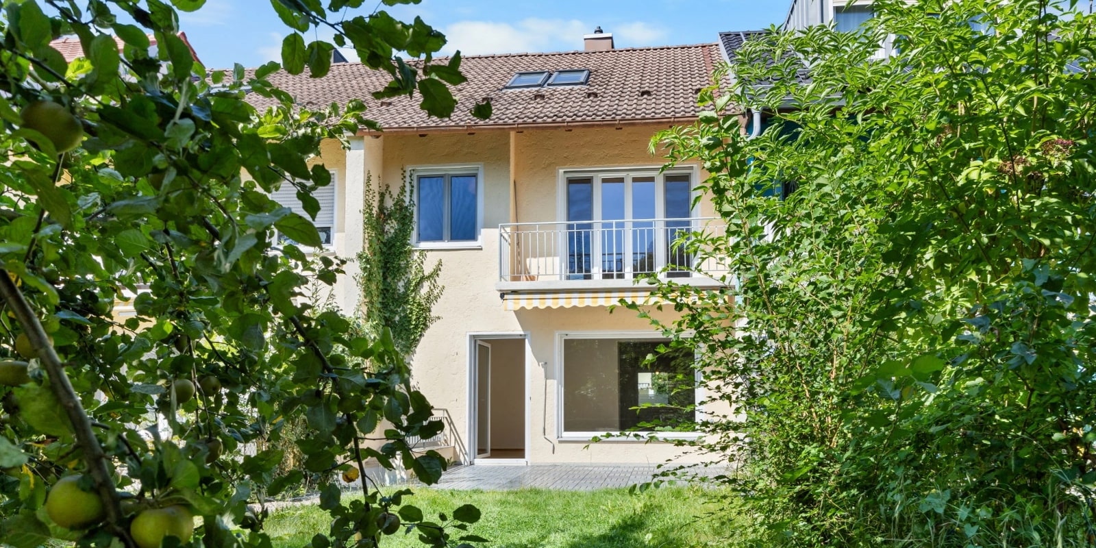 Reihenmittelhaus mit gepflegtem Garten, umrahmt von Apfelbaumzweigen im Vordergrund