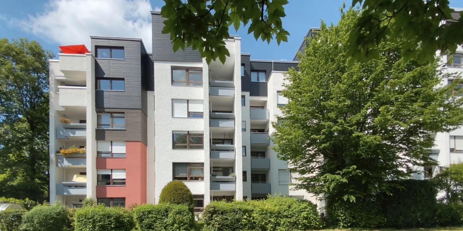 Mehrfamilienhaus mit Balkonen und rotem Fassadenakzent in einer Siedlung in München-Hadern