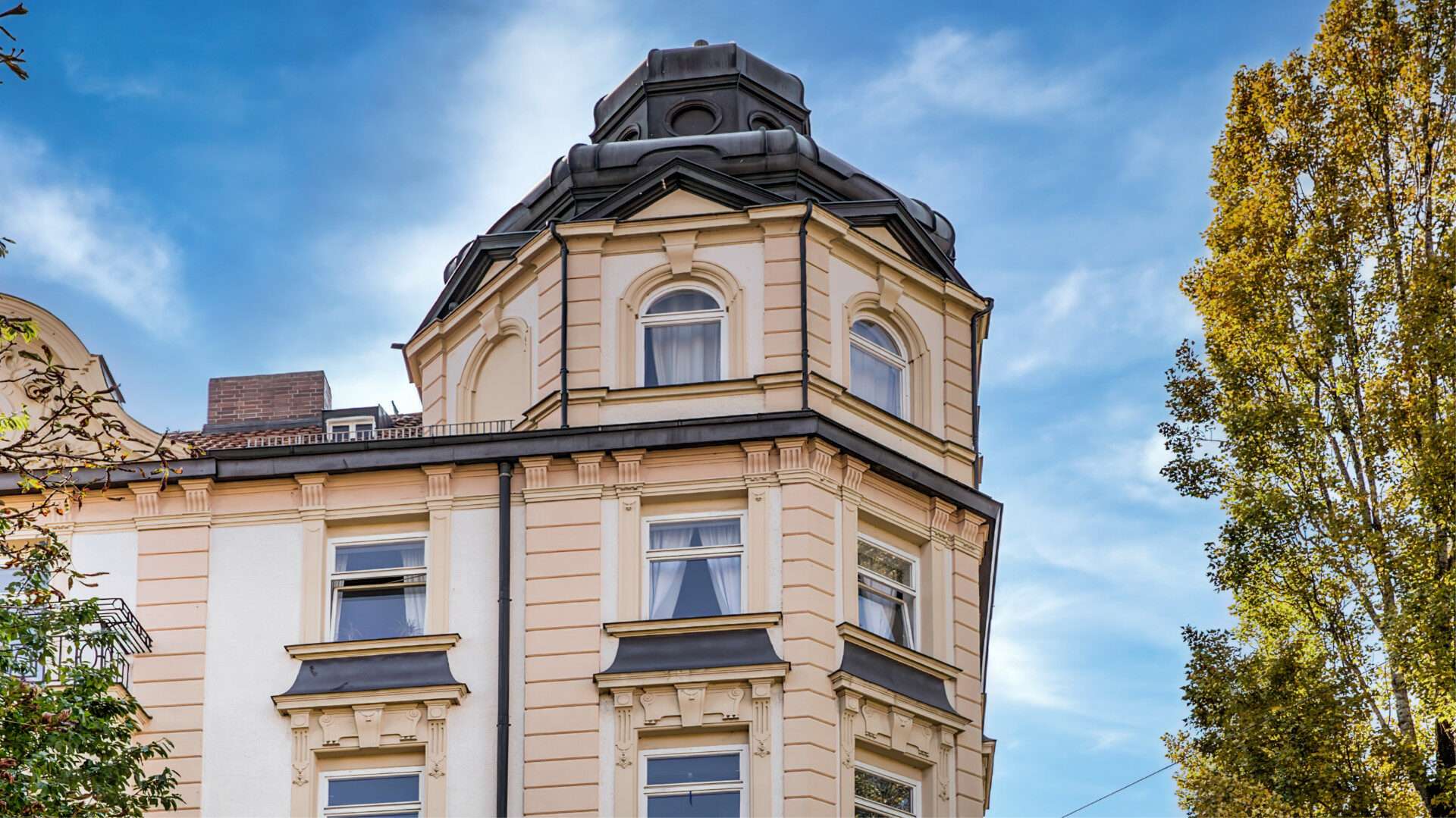 Cremefarbener Altbau mit rundem Turmerker und dunklem Kuppeldach im Münchner Stadtteil Au