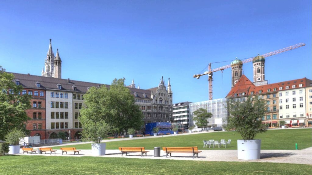 Grünanlage in der Münchner Innenstadt mit Baukränen und Blick auf historische Kirchtürme im Hintergrund