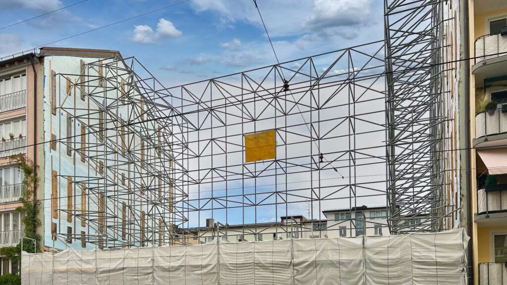 Baustelle mit eingerüstetem Gebäude und Schutznetz in einer Münchner Straße