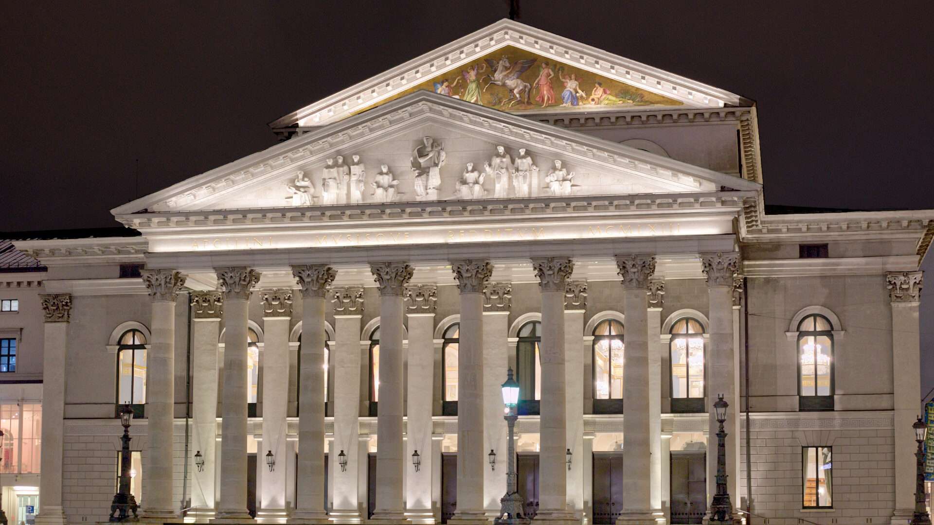 Beleuchtete Fassade der Bayerischen Staatsoper mit Säulen bei Nacht im Münchner Stadtteil Lehel