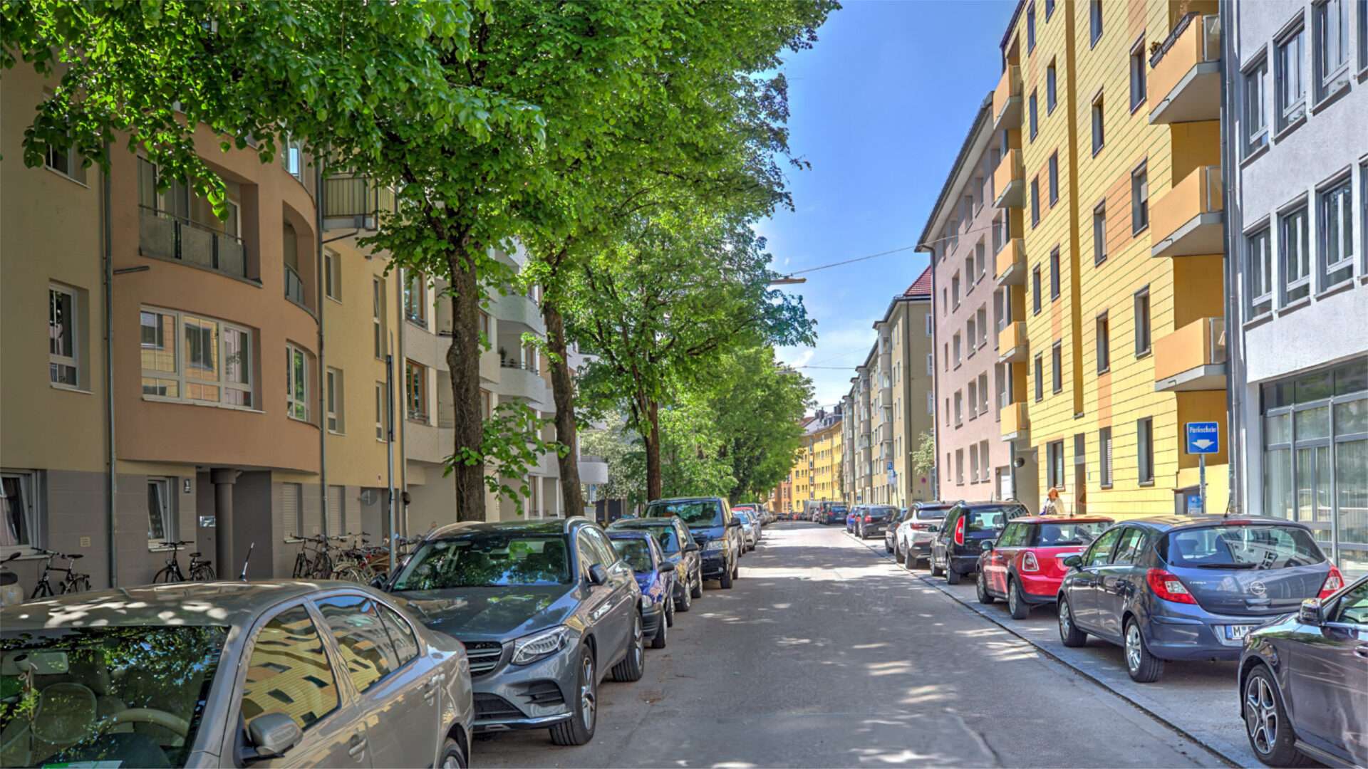 Baumbestandene Bruderhofstraße mit bunten Fassaden und parkenden Autos im Münchner Stadtteil Sendling