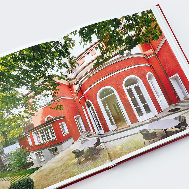 Aufgeschlagenes Buch mit Fotografie einer roten Villa mit Säulen und Gartenmöbeln