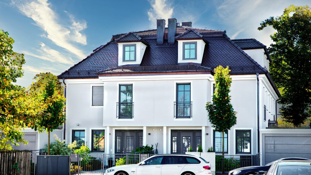 Neu gebautes weißes Doppelhaus mit Gauben und parkenden Autos in einer Münchner Wohnstraße