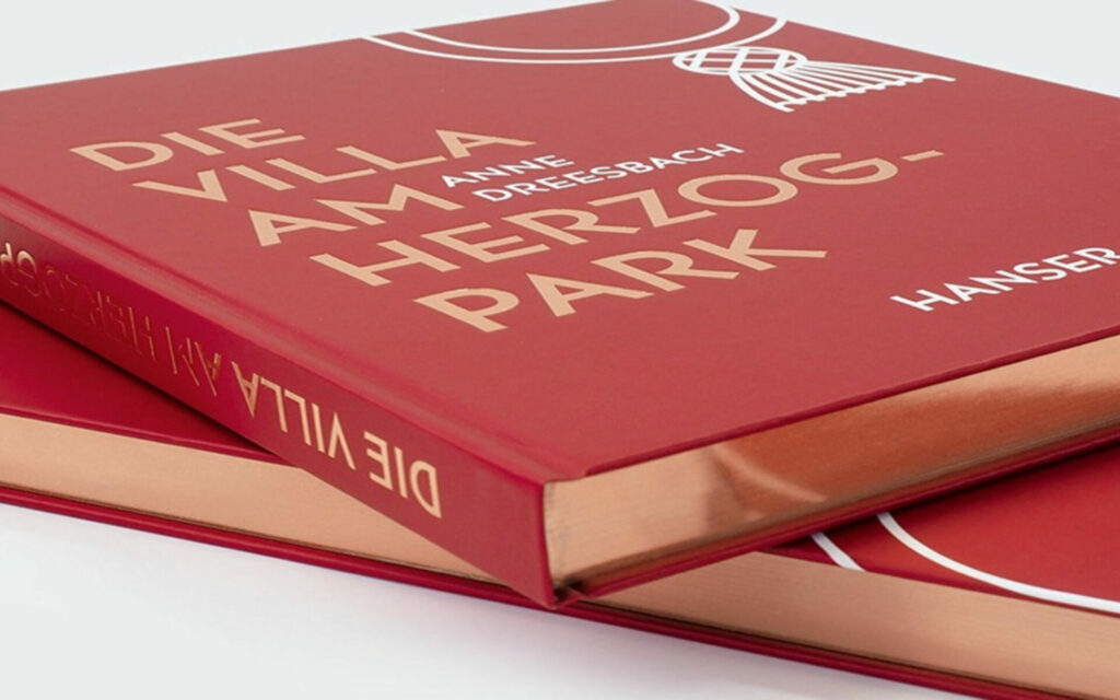 Zwei gestapelte rote Exemplare des Buches 'Die Villa am Herzogpark' aus dem Carl Hanser Verlag