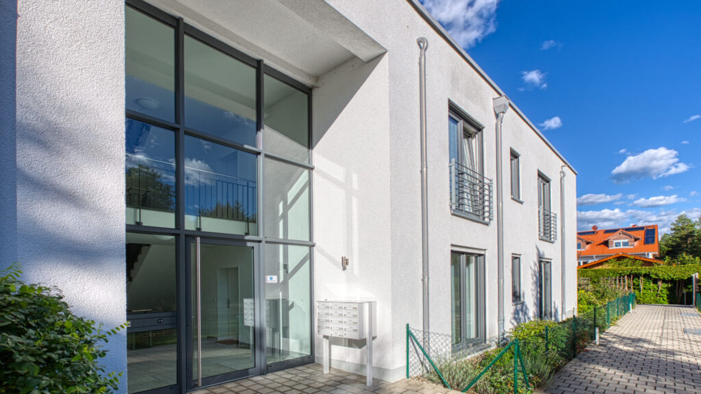 Modernes Wohnhaus mit großen Glasfronten, Terrasse und Grünbepflanzung im Sonnenlicht