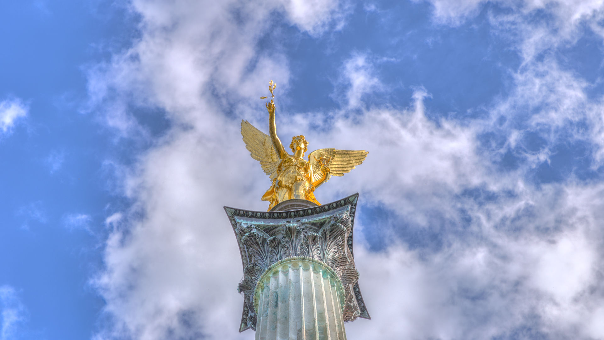 Goldene Friedensengel-Statue auf Säule vor Wolkenhimmel im Münchner Stadtteil Bogenhausen