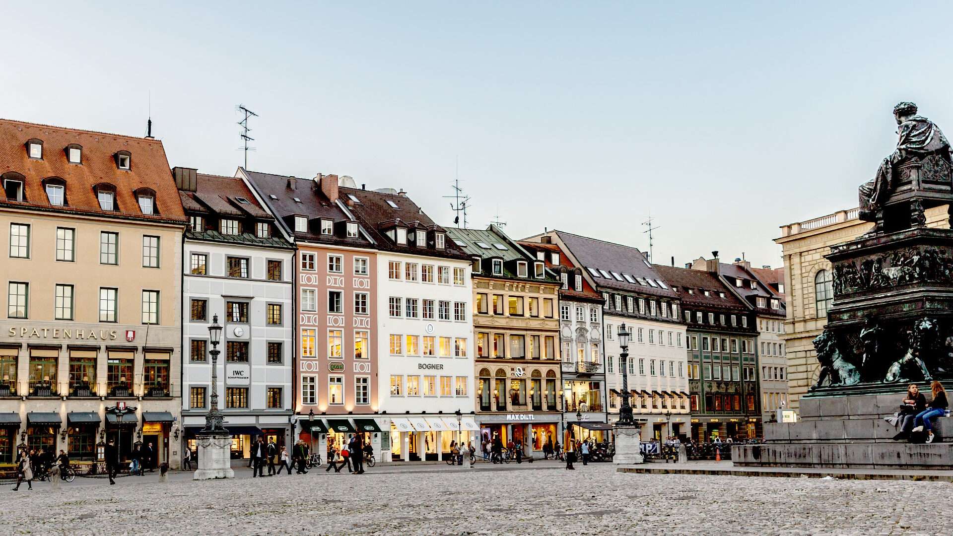 Bunte historische Geschäftshäuser an einem Platz mit Denkmal im Münchner Stadtteil Lehel