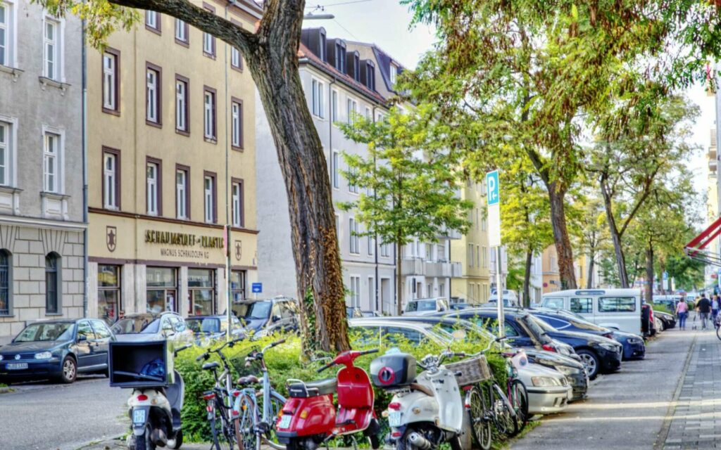 Münchner Straßenszene mit parkenden Autos, Rollern und Altbaufassaden