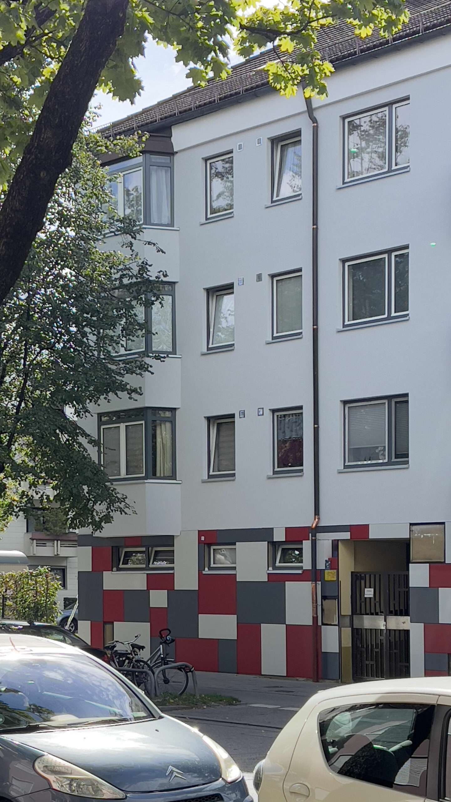 Modernisiertes weißes Wohnhaus mit rot-weiß gemusterter Fassade im Münchner Stadtteil Harlaching