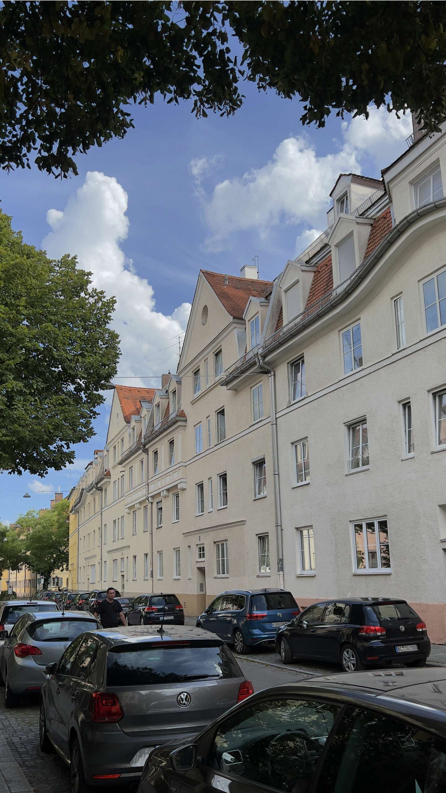 Cremefarbene Wohnhauszeile mit Gauben und parkenden Autos im Münchner Stadtteil Harlaching
