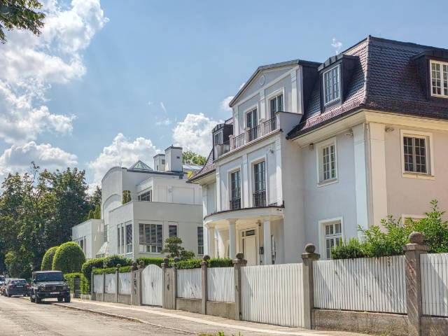 Weiße klassizistische Villen hinter Zaun an einer Münchner Straße – Symbolbild zum Hausverkauf in München