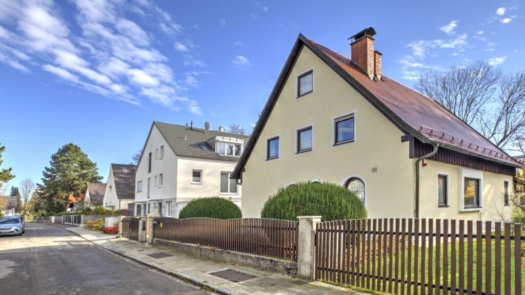 Freistehendes Einfamilienhaus mit rotem Satteldach neben einem weiteren Wohnhaus in einer Straße