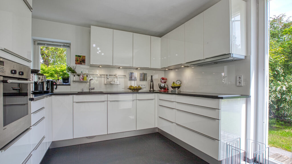 Modern gestaltete weiße Einbauküche mit dunkler Arbeitsplatte in heller Wohnung
