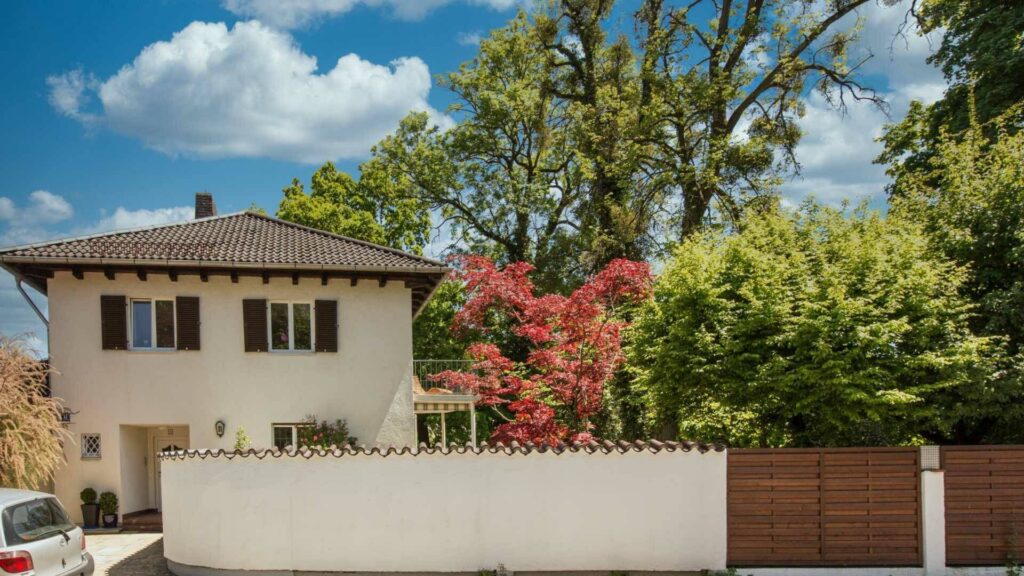 Cremefarbenes Haus mit blühendem rosa Baum und weißer Gartenmauer