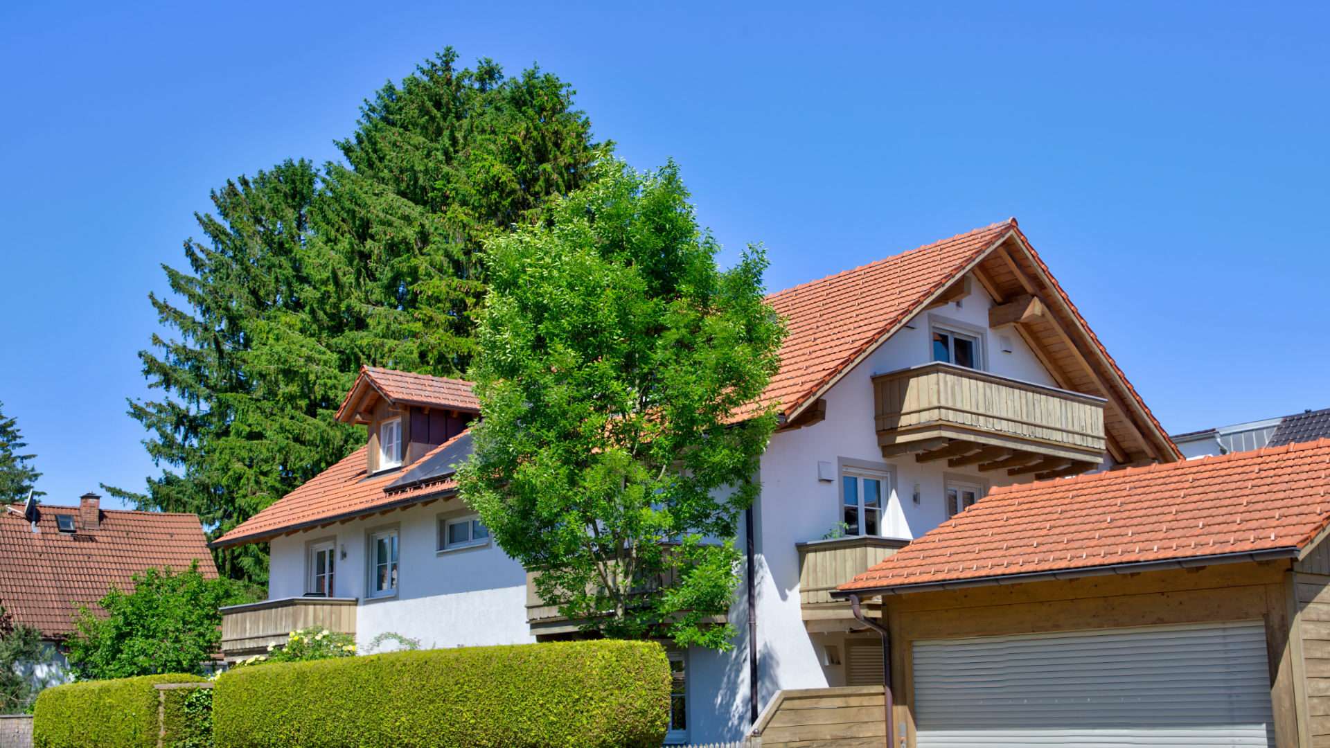 Mehrfamilienhaus mit rotem Ziegeldach und Hecke hinter hohem Nadelbaum in München-Aubing