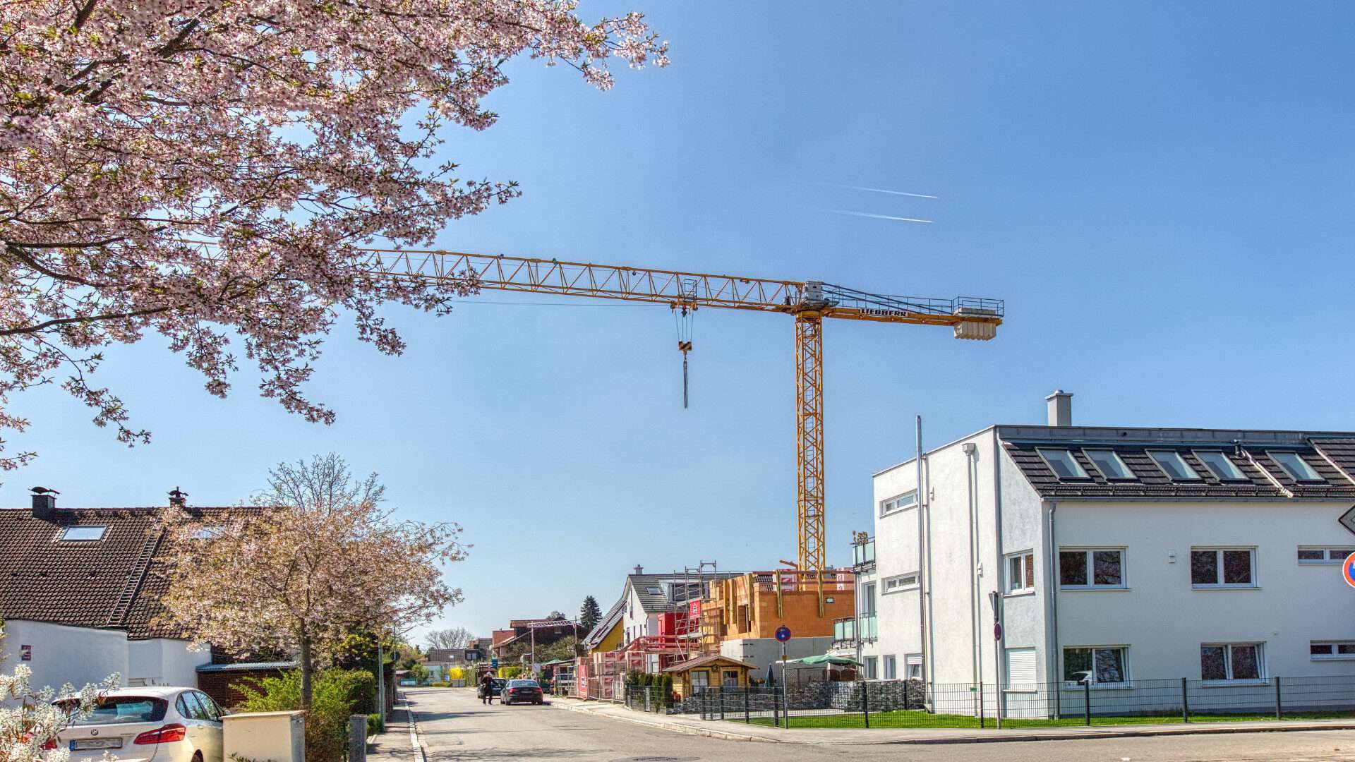 Kran an einer Neubau-Baustelle neben blühendem Kirschbaum in Germering bei München