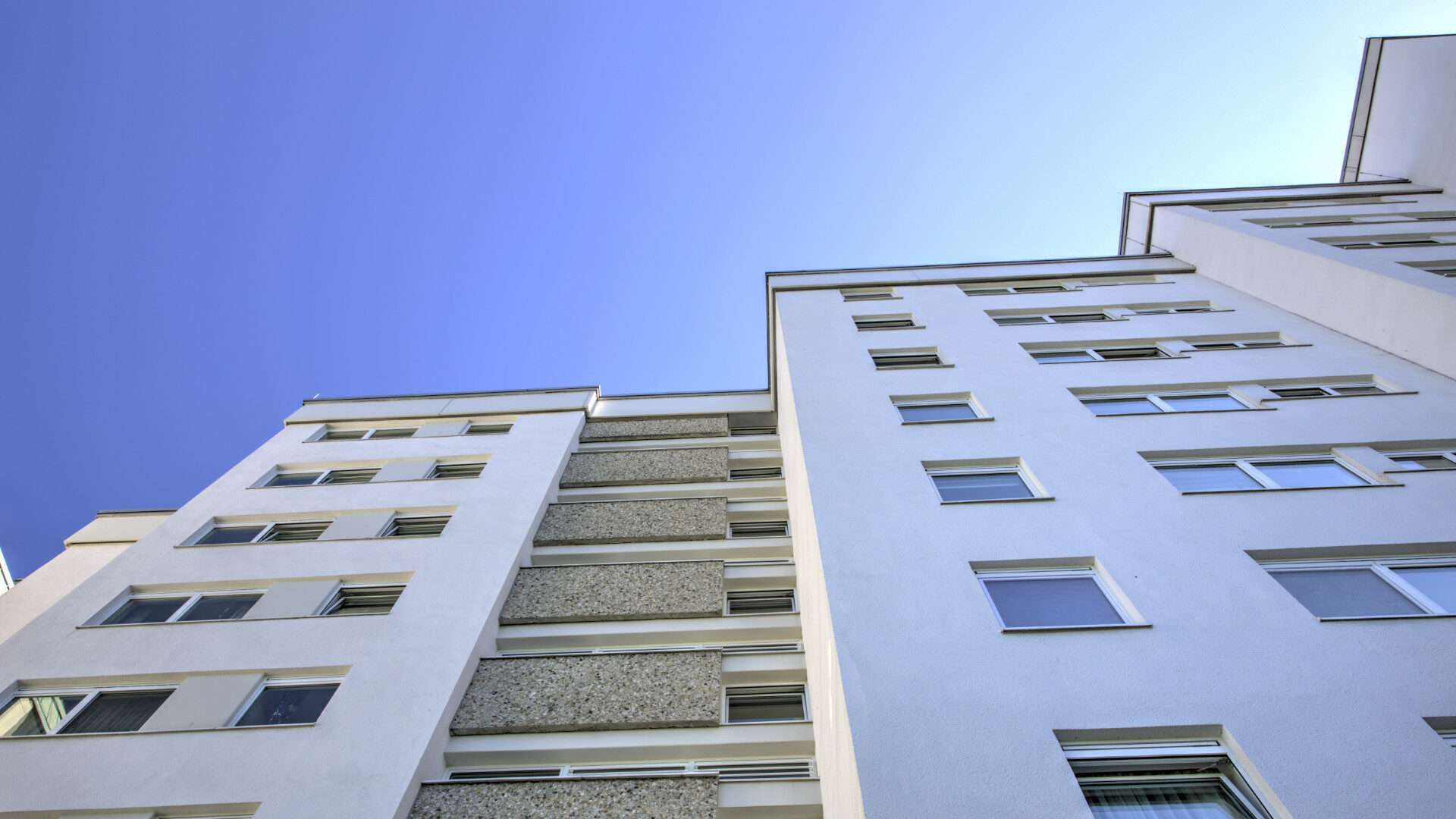 Blick von unten auf ein hohes Wohngebäude mit vielen Fensterreihen vor blauem Himmel in Germering bei München