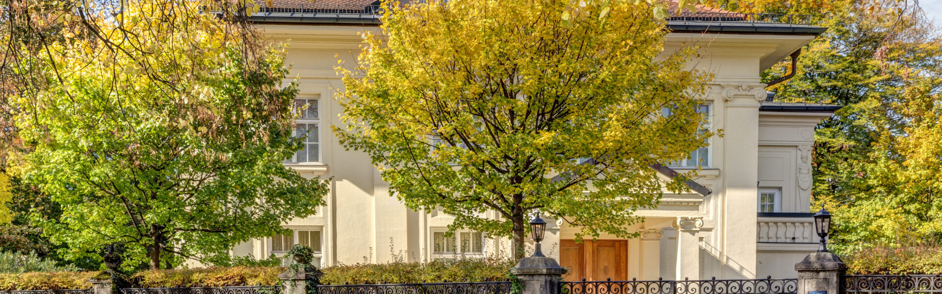 Cremefarbene Villa mit gelb verfärbten Herbstbäumen im Münchner Stadtteil Harlaching