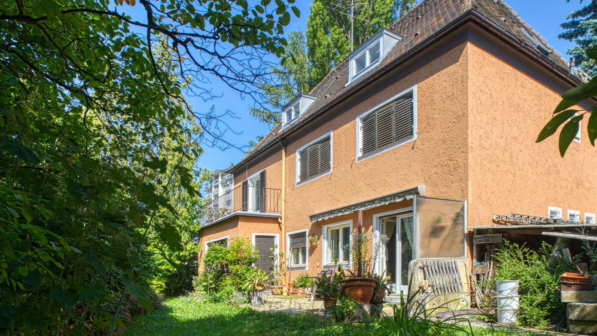 Ockerfarbenes Altbauhaus mit Fensterläden und grünem Grundstück im Münchner Stadtteil Laim