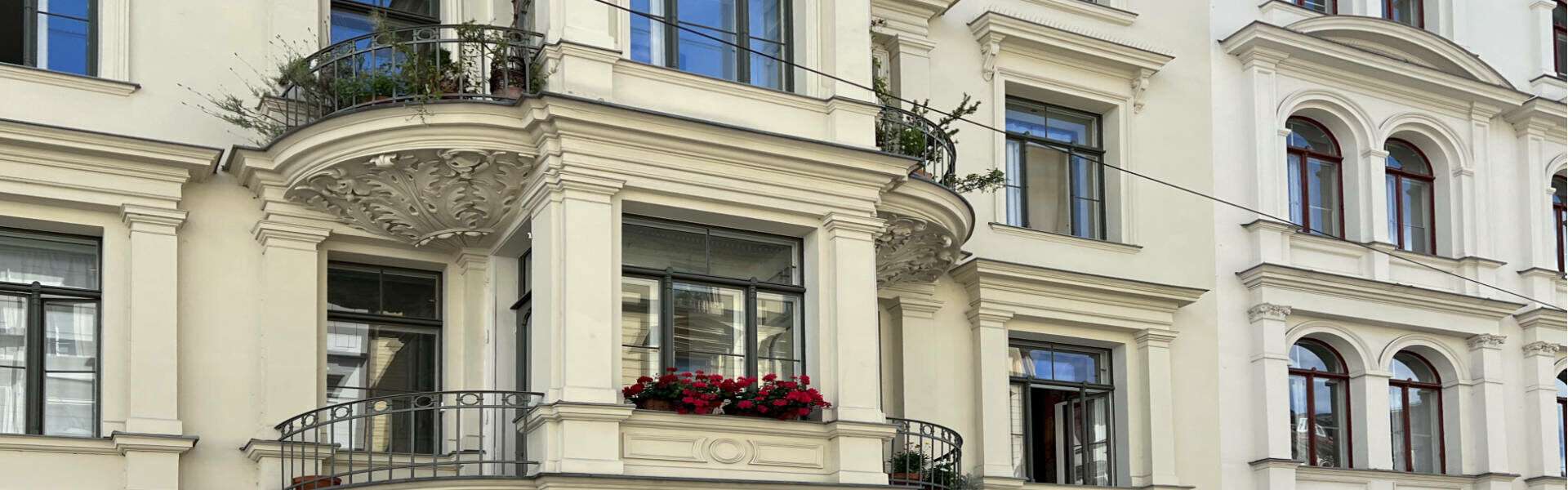 Altbaufassade mit rundem Balkon und roten Blumen im Münchner Stadtteil Au – Symbolbild zum Immobilienmakler