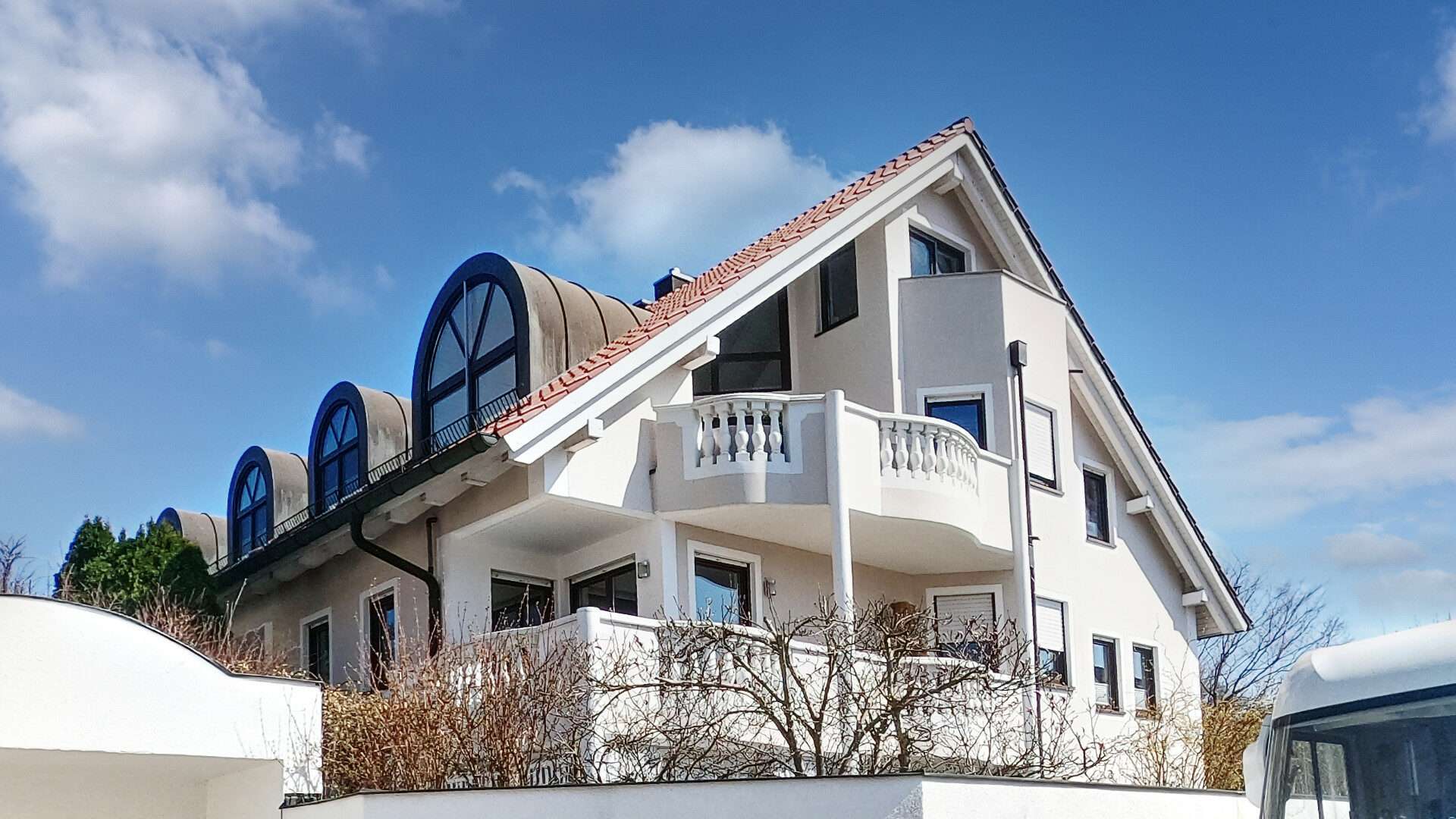 Weiße Villa mit geschwungenen blauen Erkerbalkonen und aufwendiger Fassadengestaltung in Neuried bei München