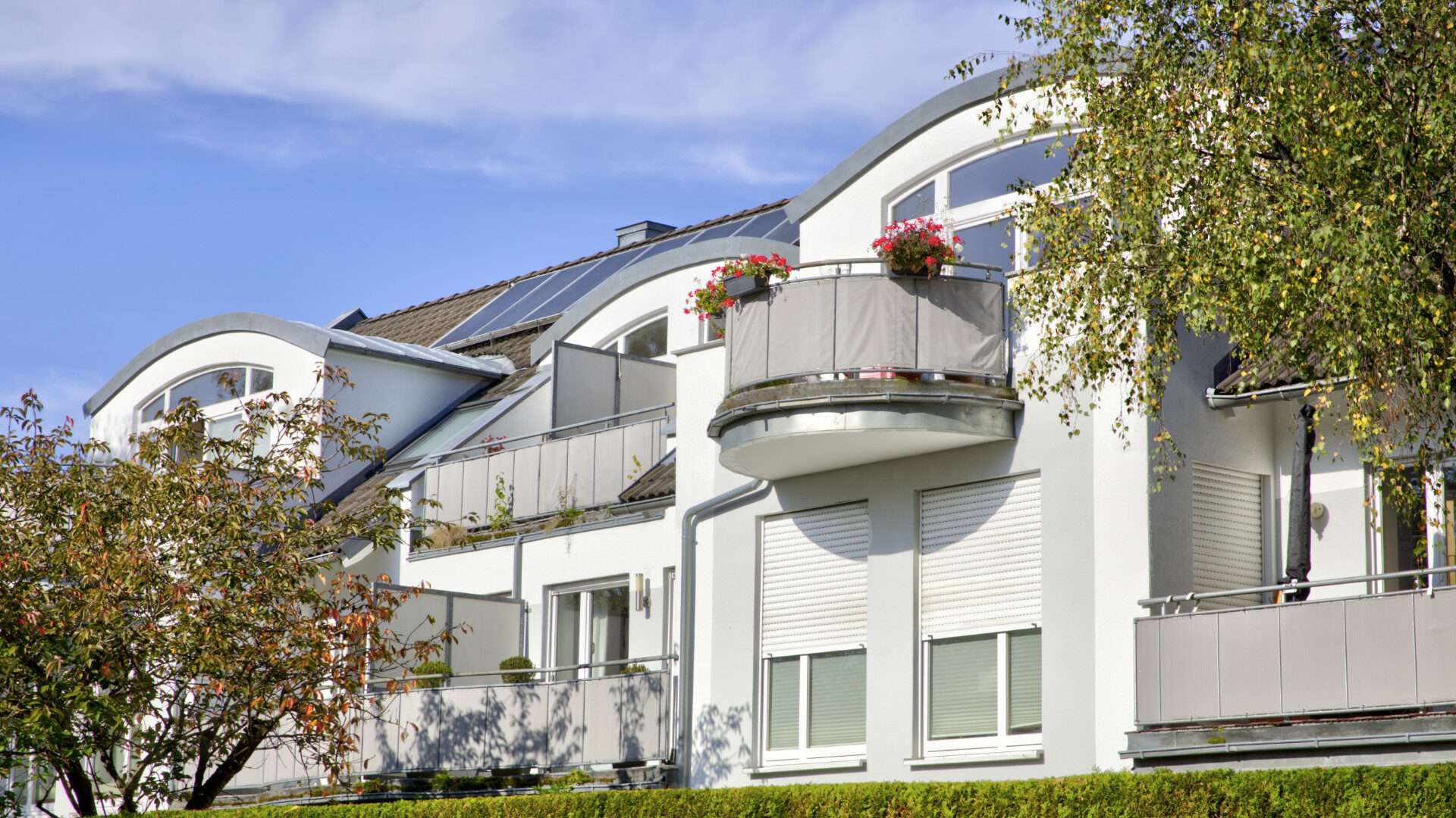 Weißes Gebäude mit geschwungenem Rundbalkon und herbstlichem Strauch im Vordergrund in München-Pasing