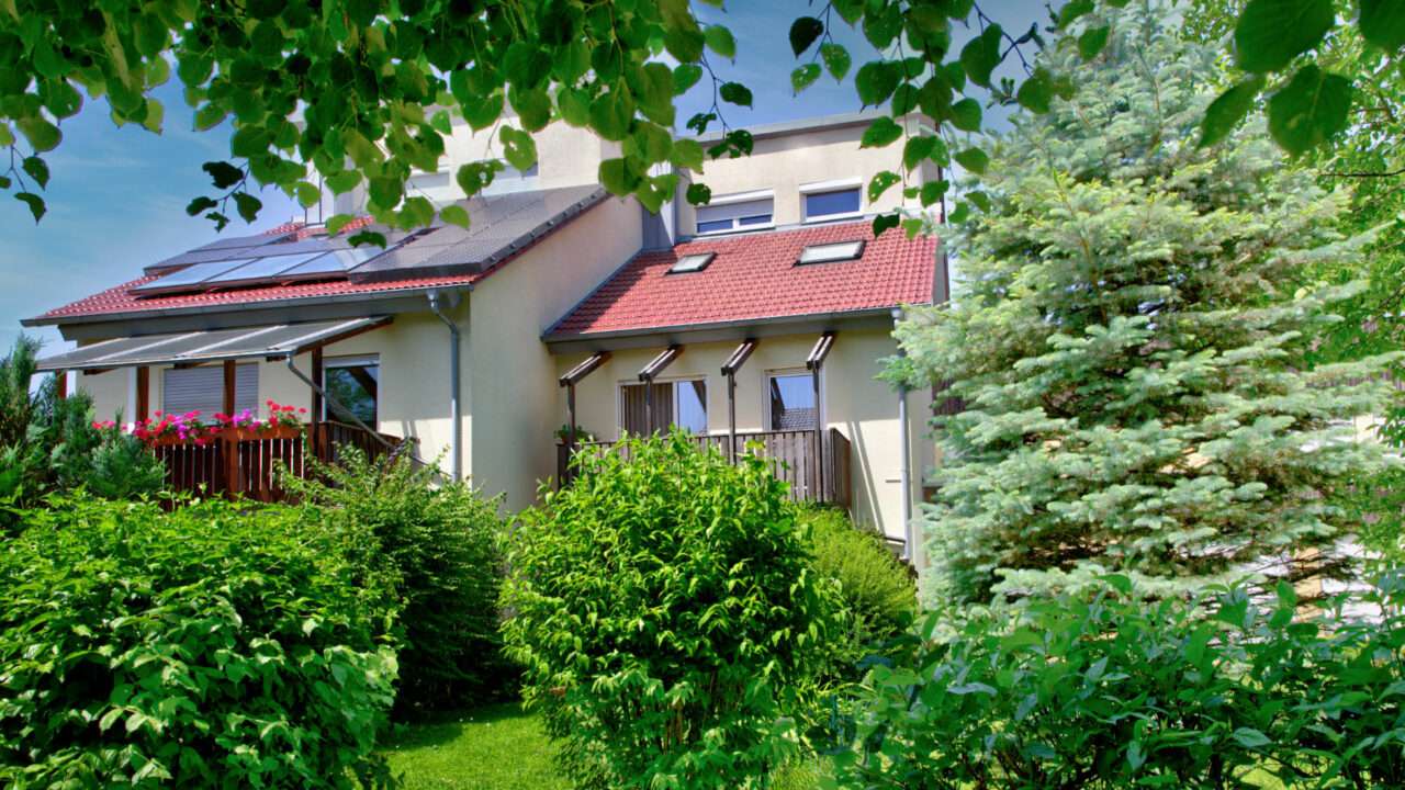 White semi-detached house with a red tile roof, solar system, and densely planted garden in Puchheim near Munich