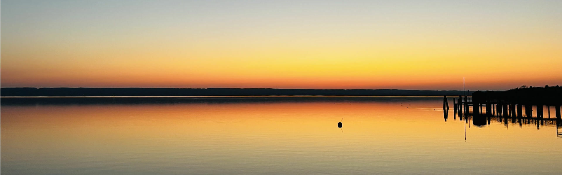 Stimmungsvoller Sonnenuntergang mit orangefarbenem Himmel über dem Wörthsee bei München