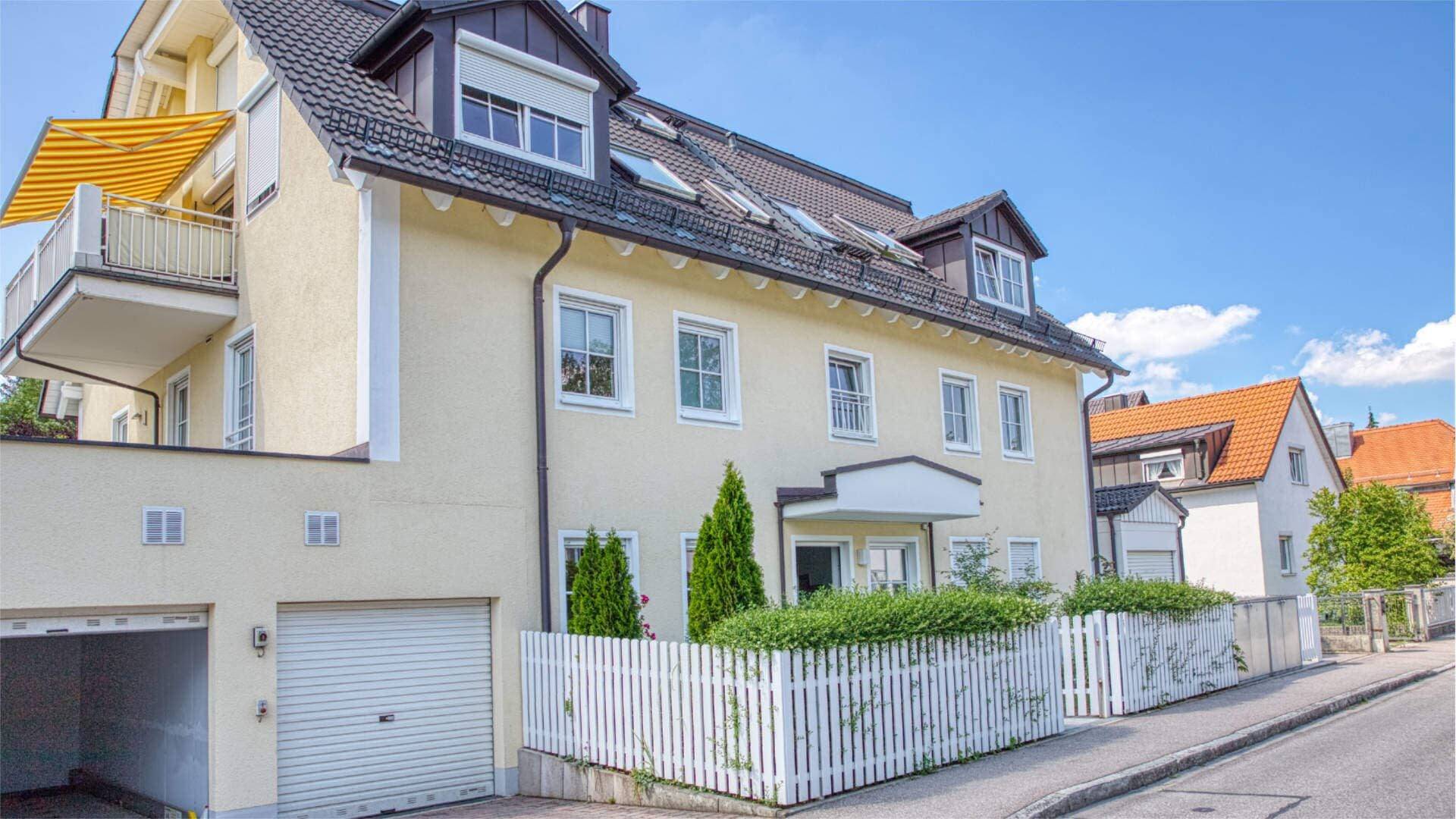 Cremefarbenes Mehrfamilienhaus mit Gaube und weißem Gartenzaun im Münchner Stadtteil Solln