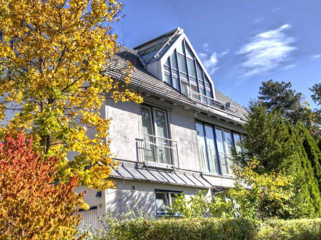 Villa mit auffälligem Glasgiebel und herbstlich gefärbten Sträuchern in München-Trudering