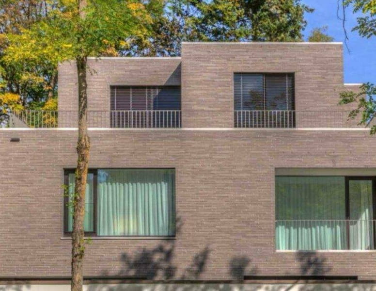 Moderne Klinkerfassade mit Balkonen und Glasgeländer, umgeben von herbstlichen Bäumen