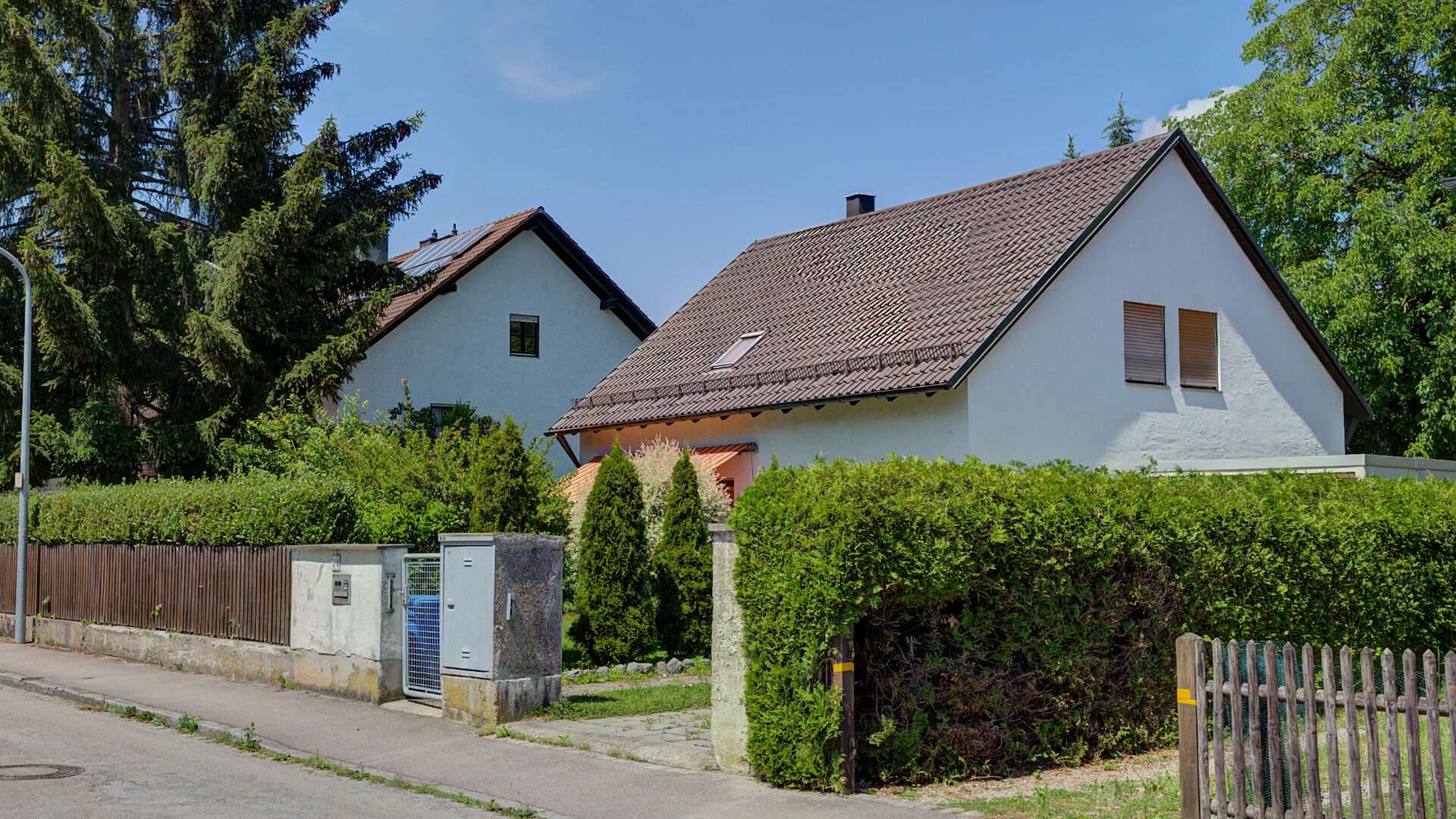 Kleines weißes Wohnhaus mit Satteldach und Hecke im Münchner Stadtteil Forstenried