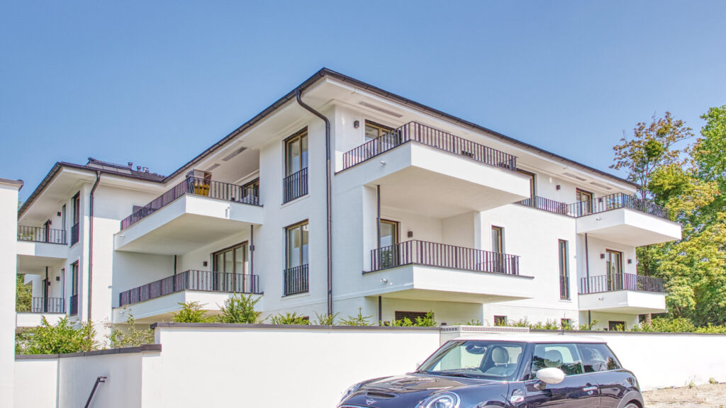 Modernes weißes Mehrfamilienhaus mit umlaufenden Balkonen und parkendem Auto davor