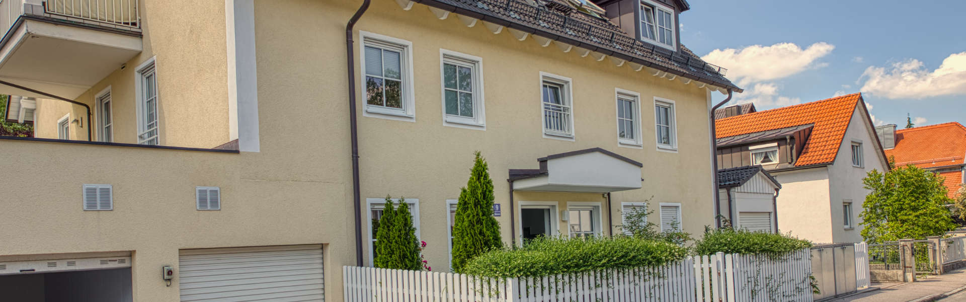 Beiges mehrstöckiges Wohnhaus mit Garagen und Zaun an einer Straße in Taufkirchen bei München