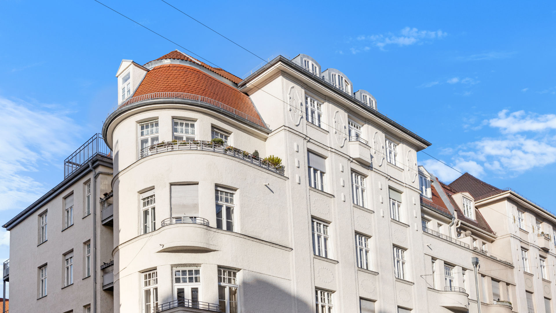Weißes Mehrfamilienhaus mit rundem Erker und rotem Ziegeldach im Münchner Stadtteil Schwabing