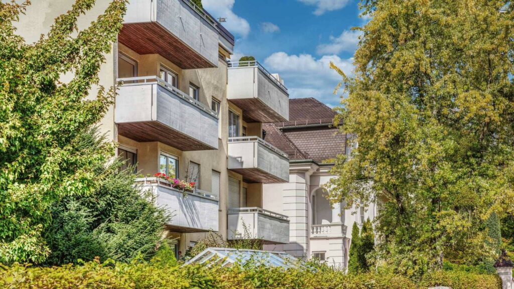 Modernes Wohngebäude mit weißen Balkonen, umgeben von dichtem Grün