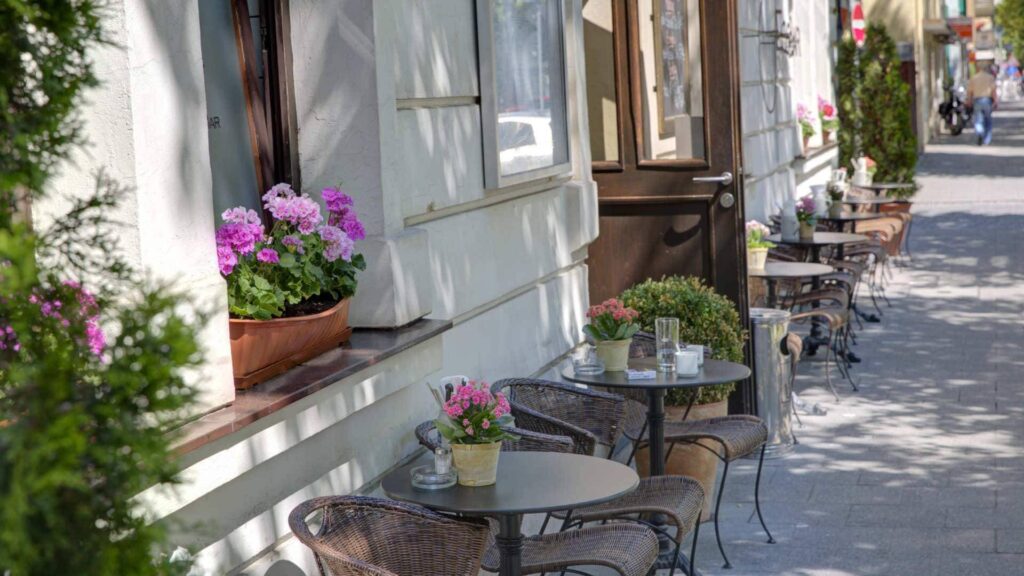 Straßencafé mit Tischen, Stühlen und blühenden Blumen vor einer Hausfassade